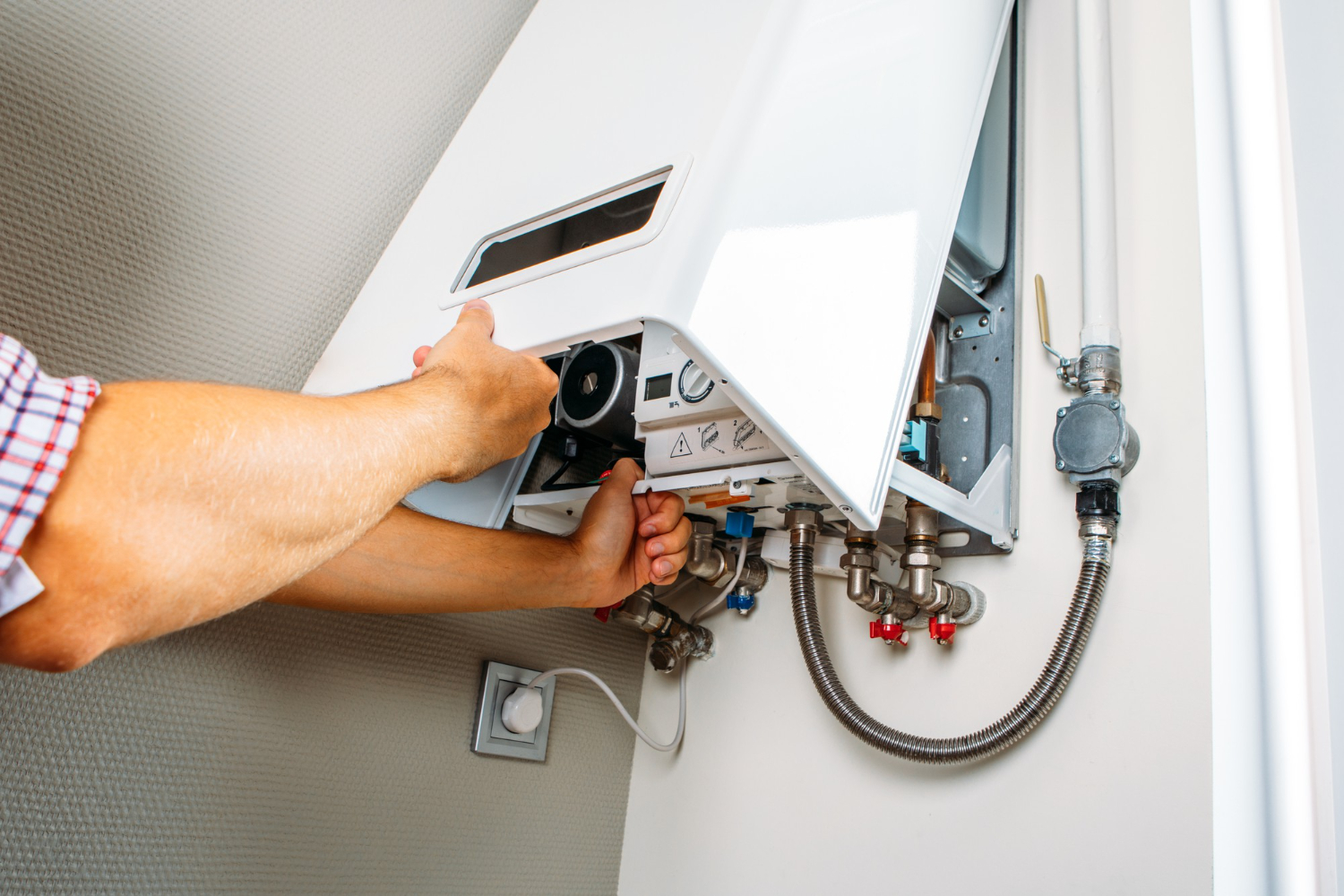 Person adjusting or repairing a wall-mounted gas boiler with the front panel open, showing pipes and controls.