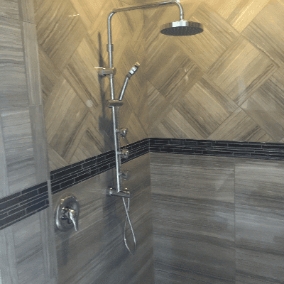 Modern shower with a rainfall showerhead, handheld sprayer, and tan tile walls with black accent stripe.