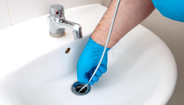 Gloved hand using a drain snake to clear a bathroom sink clog.