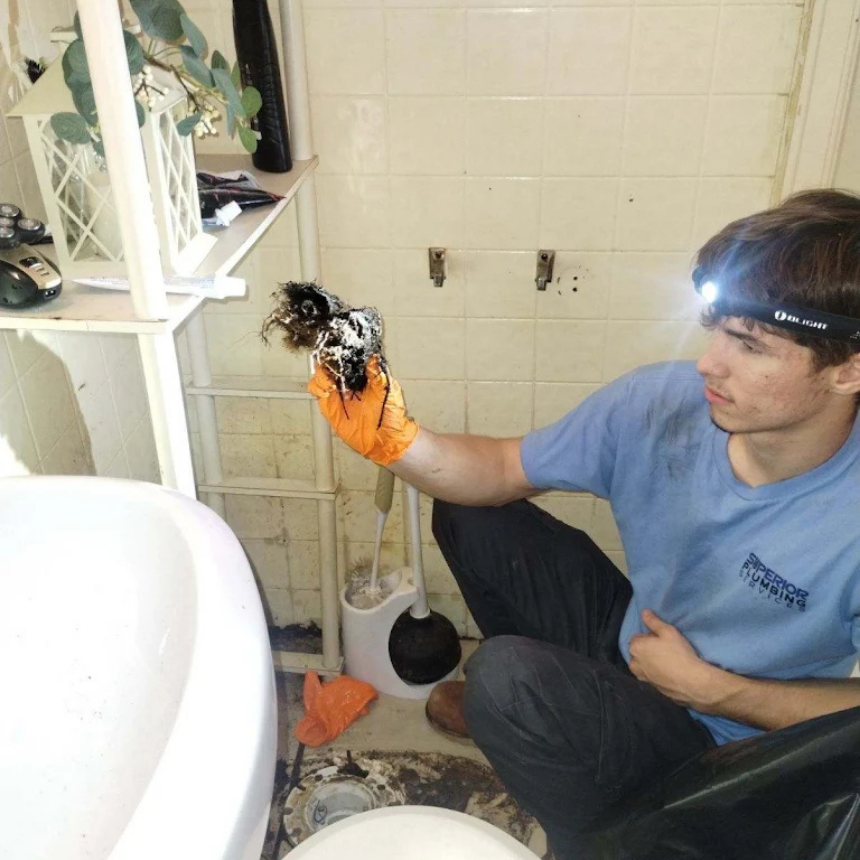 Plumber wearing a headlamp holds a clump of hair and debris removed from a bathroom drain.