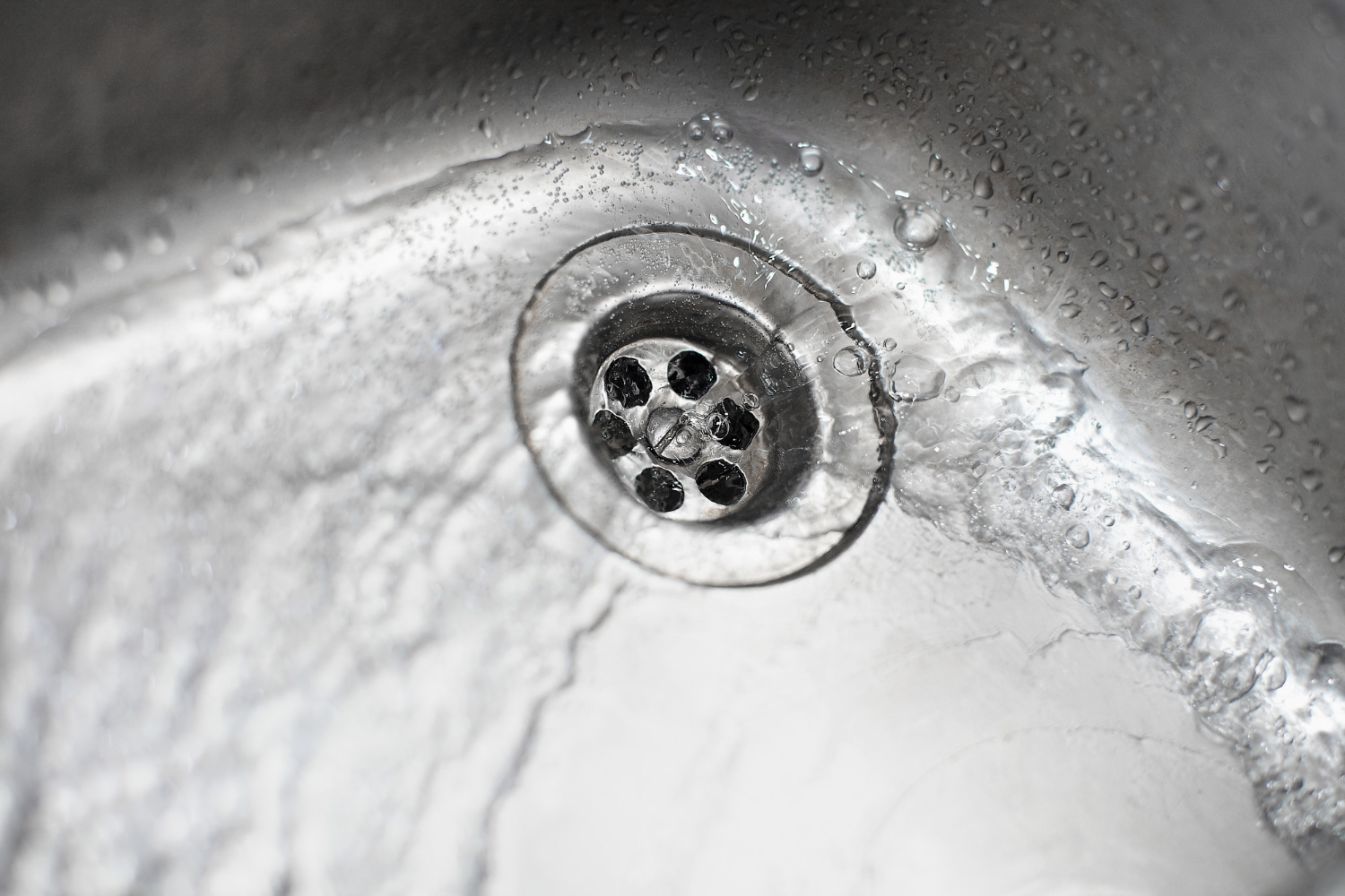 Close-up of a stainless steel sink drain with water droplets and flowing water around it.